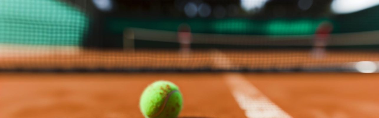 Balle de tennis sur terre battue près du filet sous la lumière naturelle.