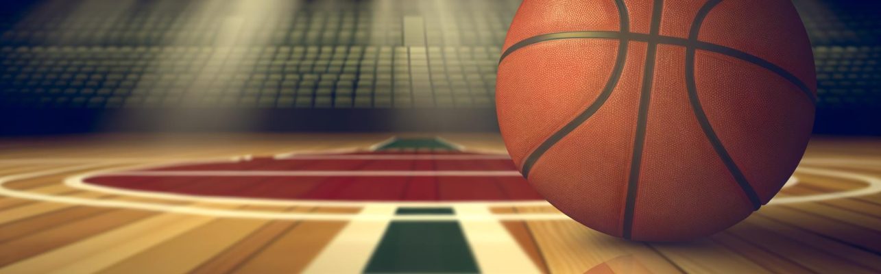 Un ballon de basket sur un terrain interieur avec des gradins vides en arriere-plan.