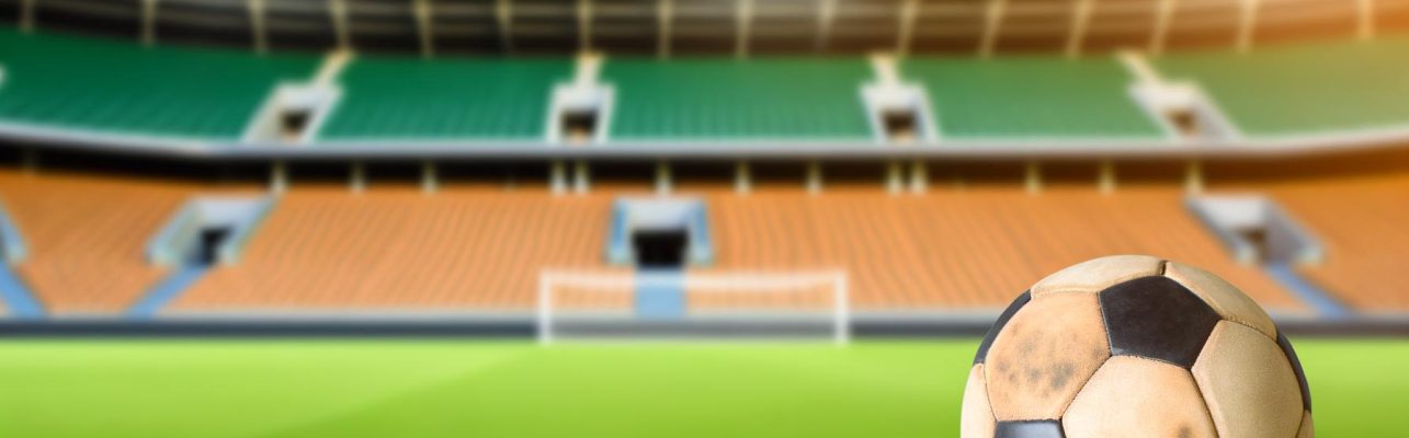 Un ballon de football use repose sur la pelouse d'un stade vide avec des sieges en arriere-plan.