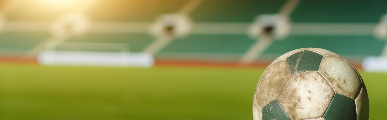 Un ballon de football usé repose sur une pelouse sous la lumière du soleil.