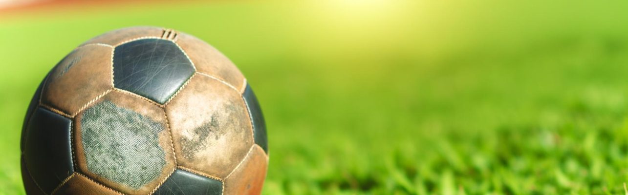 Un ballon de football usé sur une pelouse sous le soleil, arrière-plan légèrement flou.