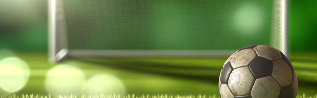 Un ballon de football usé repose sur une pelouse verte avec des buts en arrière-plan.