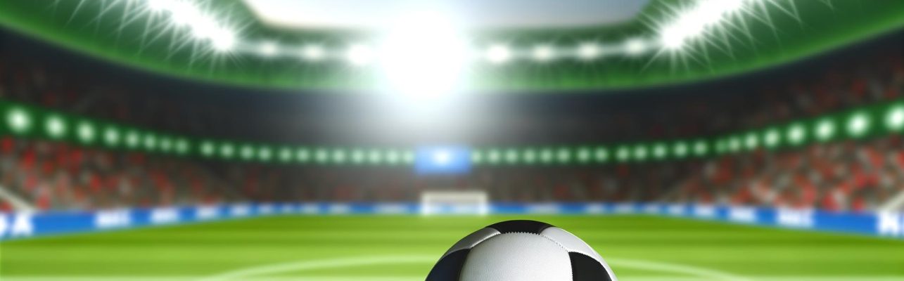 Un ballon de football use repose sur l'herbe verte d'un terrain de football avec des buts flous en arriere-plan.