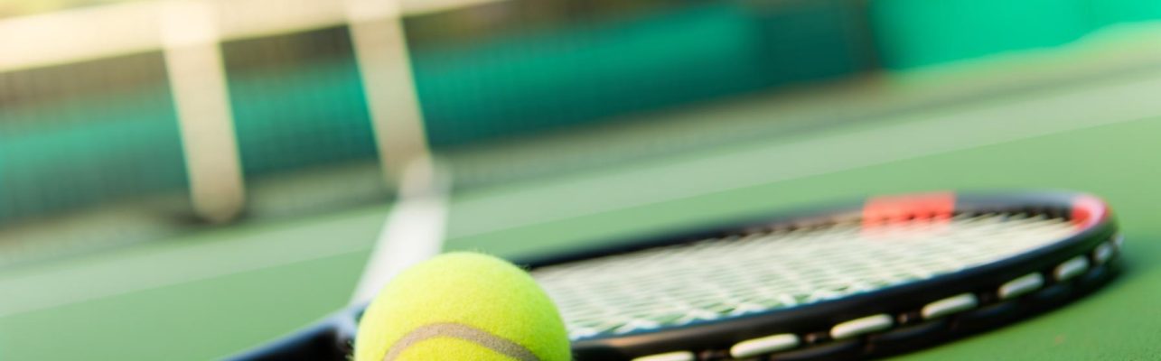 Un court de tennis avec une balle et une raquette sur la surface verte, le filet visible en arrière-plan.