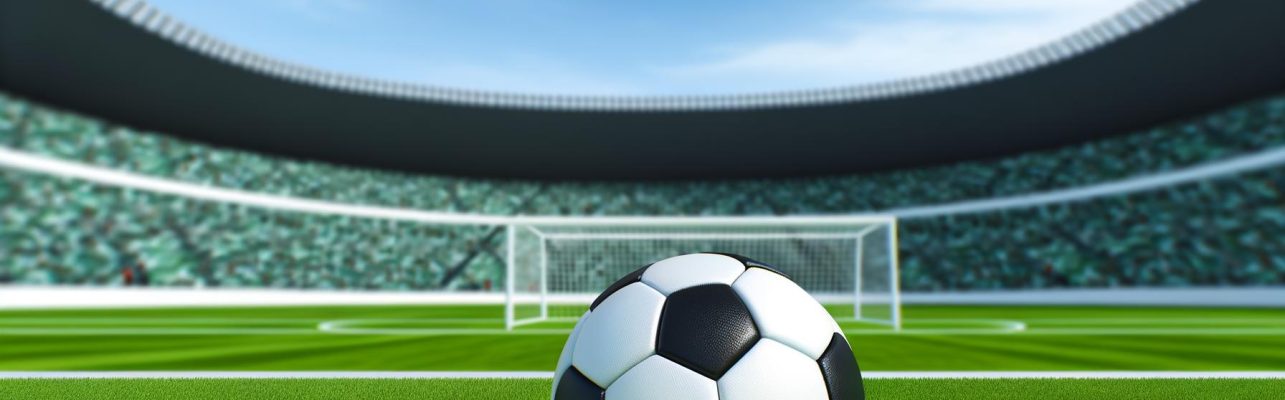 Un ballon de soccer classique repose sur une herbe fraîchement coupée dans un stade avec des sièges vides et des poteaux de but en arrière-plan.