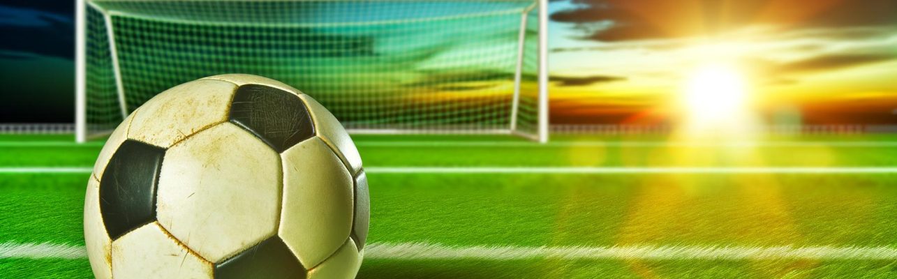Ballon de soccer sur une pelouse verte au coucher du soleil.