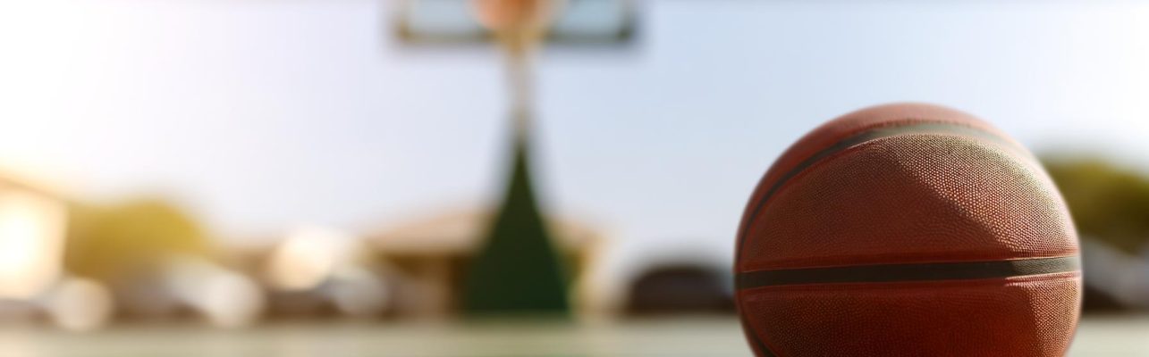 Un ballon de basket repose sur le sol en bois devant un panier en arriere-plan.