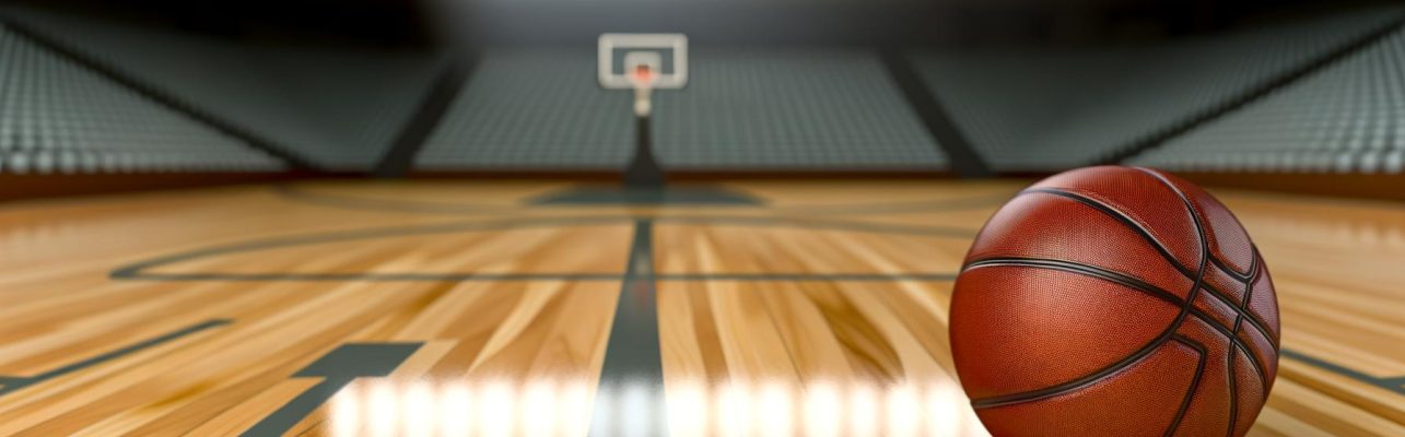 Un ballon de basketball reposant sur un sol en parquet avec des lignes de terrain visibles en arrière-plan flou.
