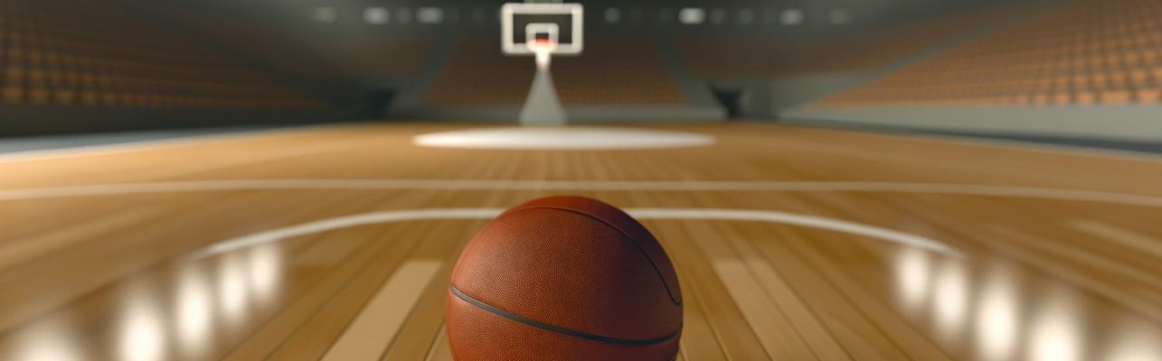 Un ballon de basket sur un sol en parquet dans une arène intérieure vide avec un panier visible au loin.