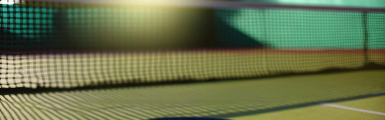 Un court de tennis le matin avec une raquette et une balle pres de la ligne de fond.