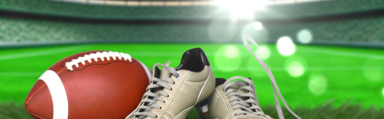 Des crampons de football usés sur de l'herbe verte avec un ballon légèrement dégonflé à proximité.