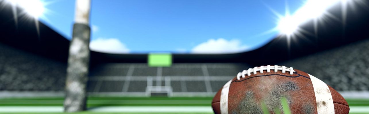 Un ballon de football sur la pelouse verte d'un terrain avec un but et des gradins en arrière-plan.