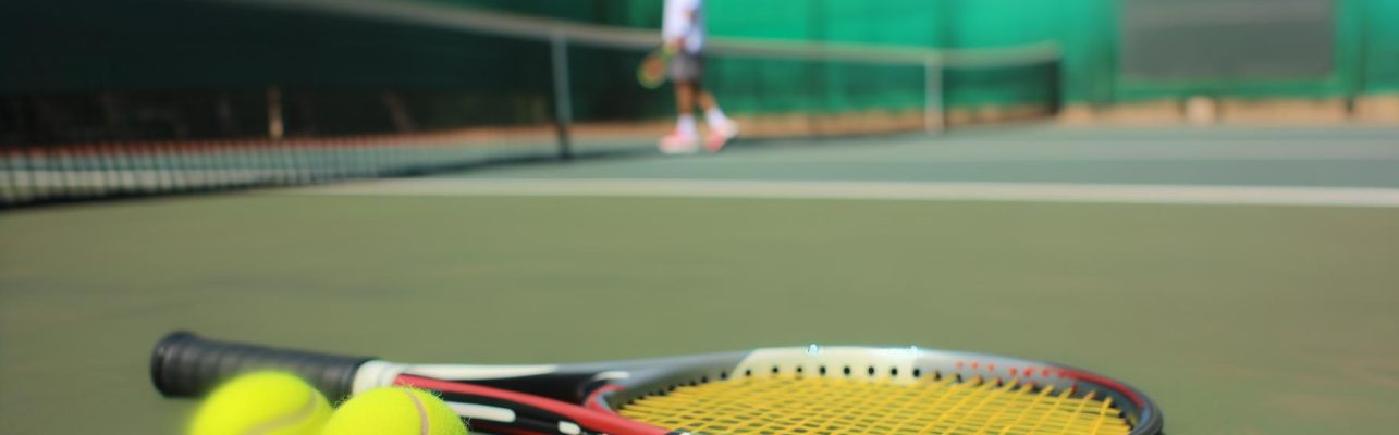 Raquette de tennis et balles sur le court avec le filet en arrière-plan.