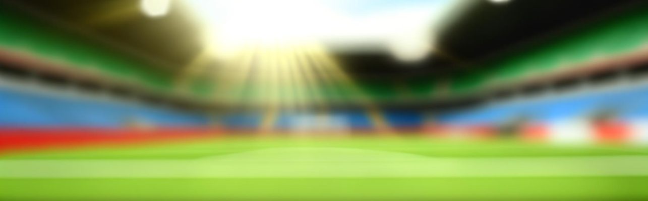 Un stade de football vu du milieu de terrain avec des gradins vides et une pelouse impeccable.