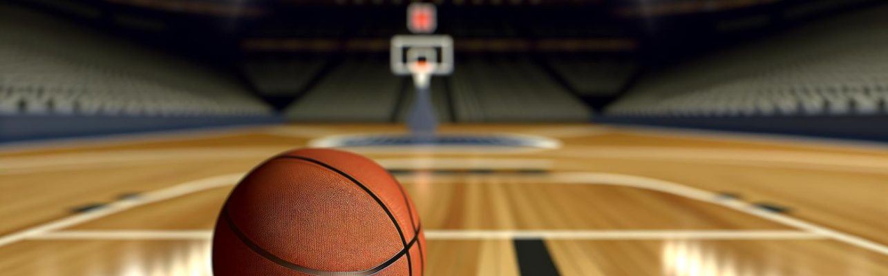 Un ballon de basket sur un parquet avec des paniers et un stade vide en fond flou.