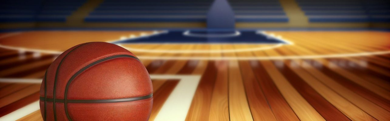 Un ballon de basket sur un terrain avec un panier en arrière-plan.