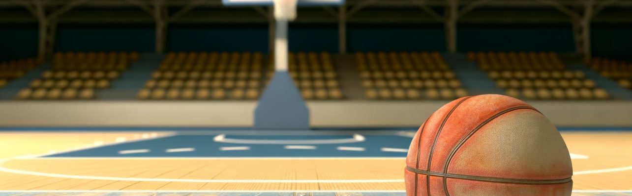 Une photo d'un terrain de basketball avec un ballon sur le sol et un panier vue de cote.