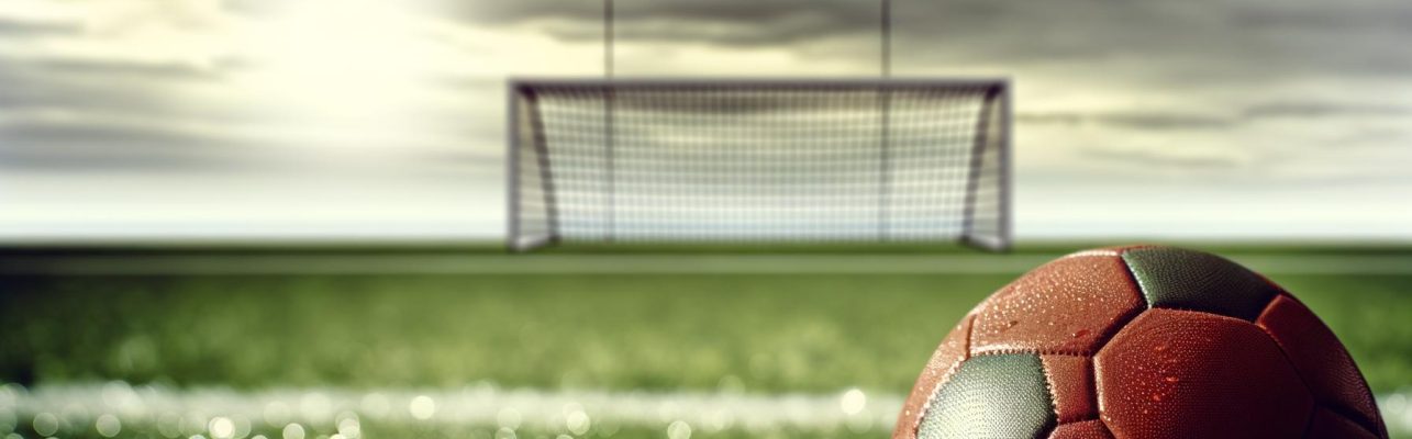Un ballon de football sur un terrain mouillé après une averse avec des buts au loin.