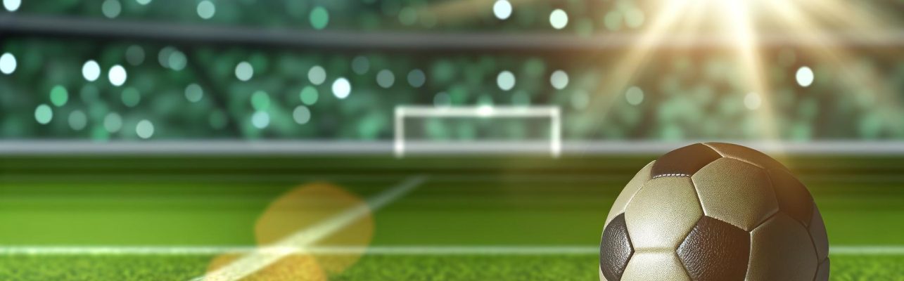 Un ballon de football en cuir sur un terrain vert avec des lignes blanches et un stade en arrière-plan.