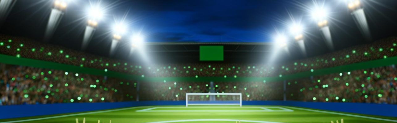 Photo d'un terrain de football avec des buts et une partie du stade à la tombée de la nuit.