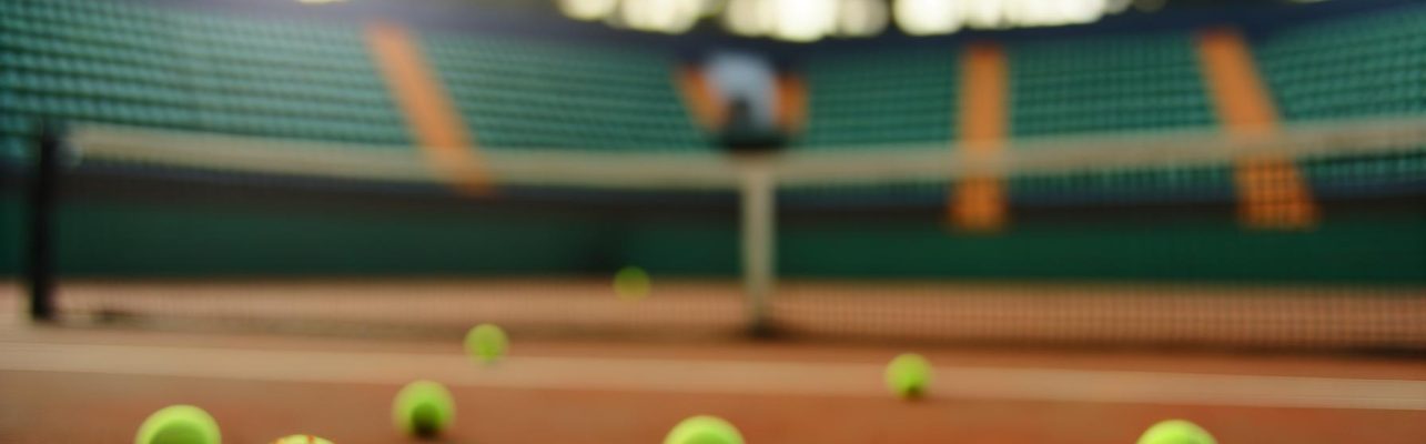 Un terrain de tennis avec filet et balles éparses sur la terre battue.