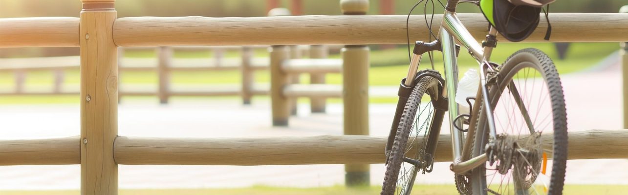 Un velo appuye contre une barriere en bois avec un casque pose sur la selle par une journee ensoleillee.